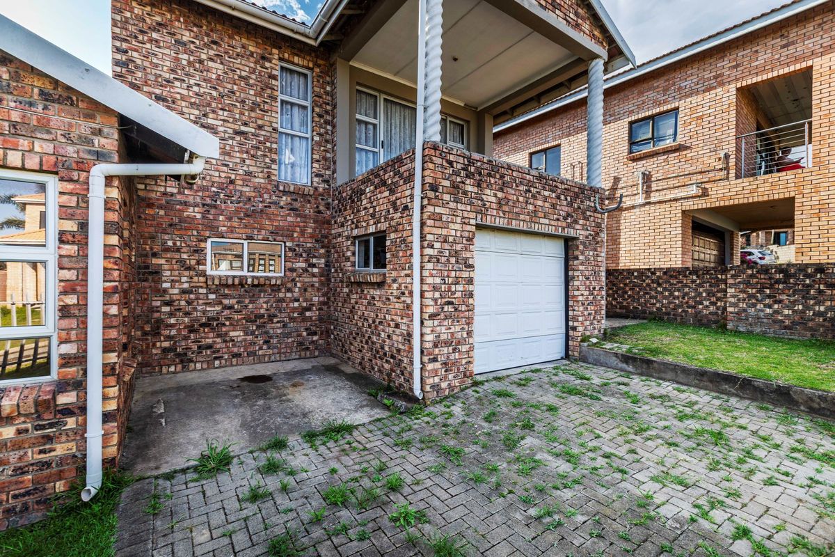 Rear exterior view of the property featuring a brick facade, a single garage, and a covered balcony area with paved driveway access.