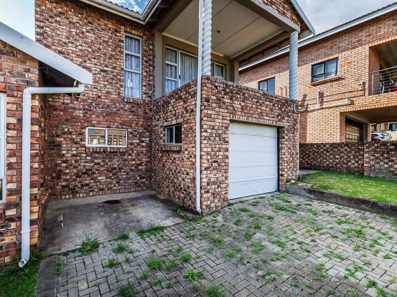 Rear exterior view of the property featuring a brick facade, a single garage, and a covered balcony area with paved driveway access.