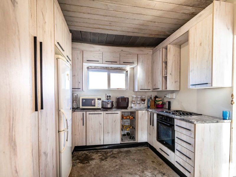 Compact kitchen featuring light wood-look cabinetry, built-in oven, hob, and an exposed timber ceiling, requiring flooring completion.