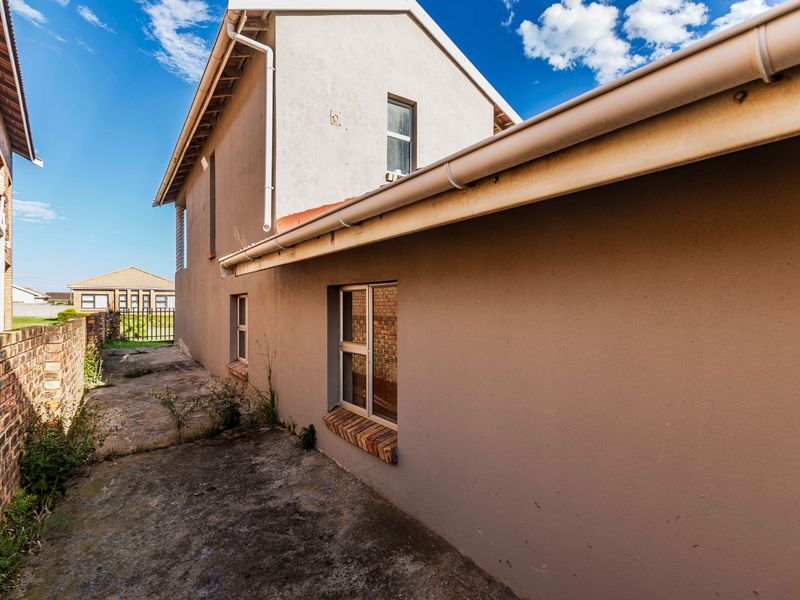 A view of the rear exterior of the house, featuring concrete paving, brick boundary walls, and standard guttering systems.