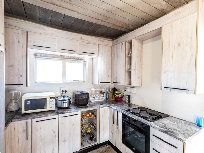A functional kitchen featuring light wood-grain cabinetry, marble-effect countertops, built-in oven and hob, and a rustic exposed timber ceiling.