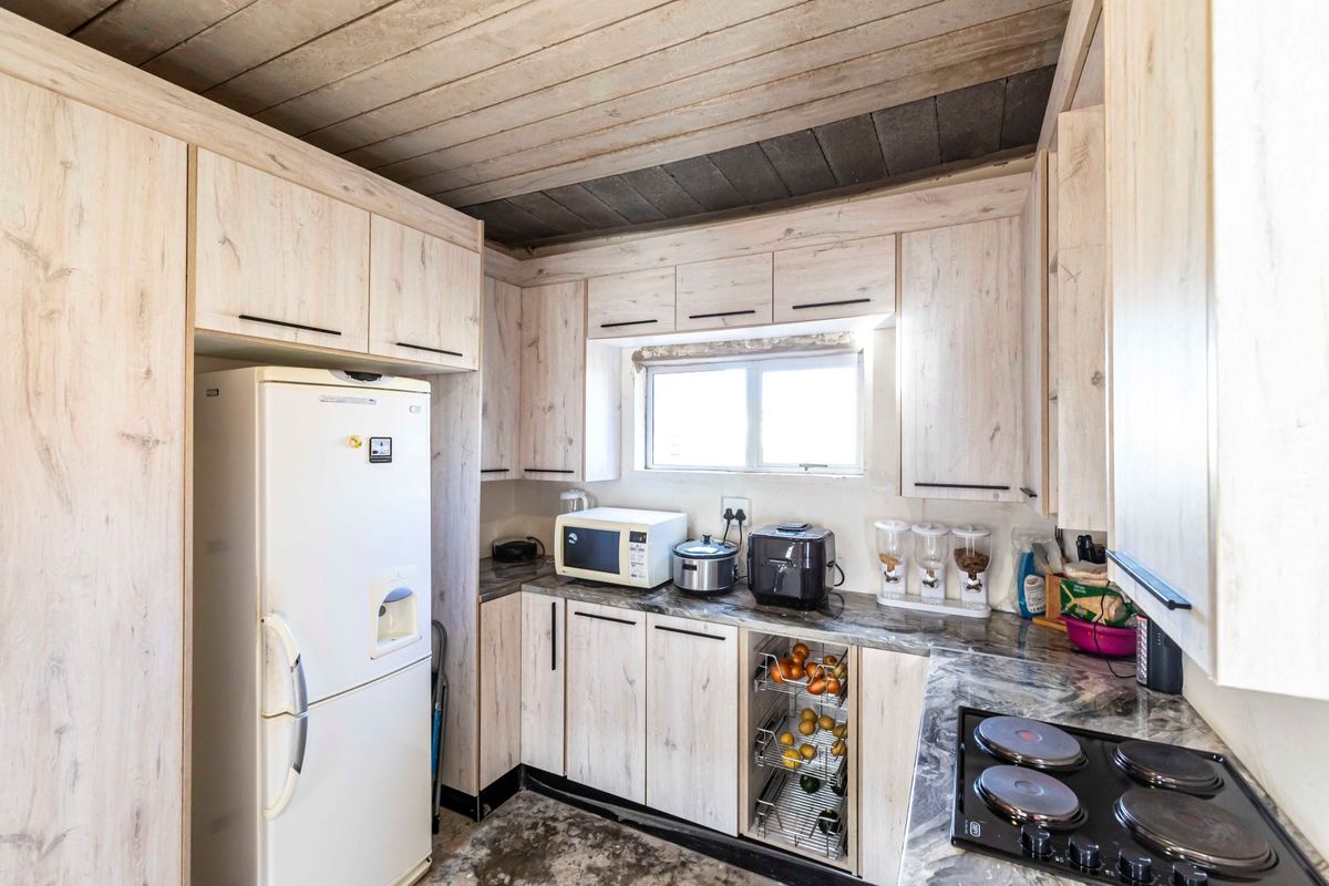 Compact kitchen featuring light wood-look cabinetry, stone-patterned countertops, an integrated electric hob, and a rustic timber-paneled ceiling.