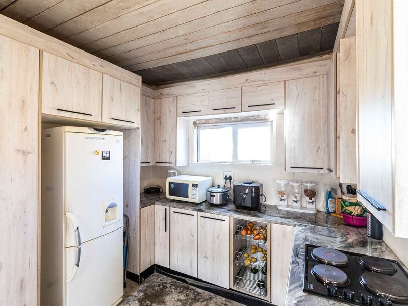 Compact kitchen featuring light wood-look cabinetry, stone-patterned countertops, an integrated electric hob, and a rustic timber-paneled ceiling.