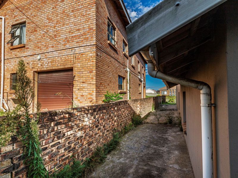 A side exterior view showing a brick facade, concrete pathway, and drainage infrastructure along the side of the property.