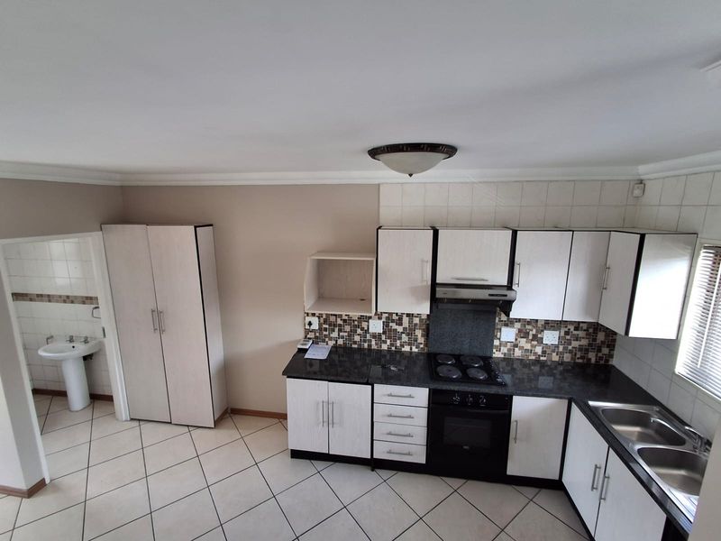 A functional kitchen featuring built-in cabinetry, granite countertops, an electric hob, and a mosaic tile backsplash, with adjacent access to a bathroom area.