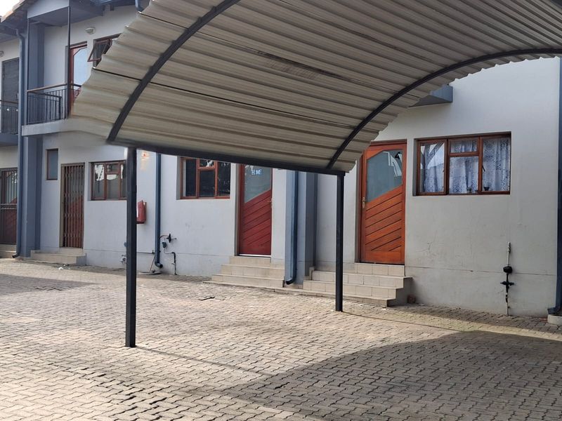 Exterior view of a townhouse complex featuring a covered carport, paved driveway, and multiple entrance doors with security features.