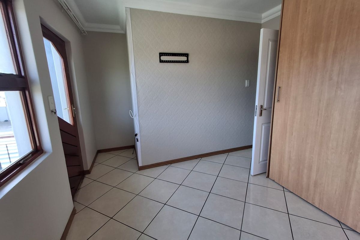 A clean, empty bedroom featuring neutral tiled flooring, built-in wooden wardrobe, and coving detail, offering a versatile space ready for personalization.