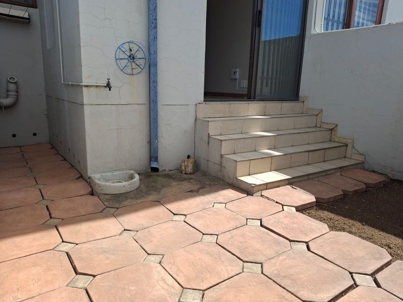 Rear exterior area featuring a tiled patio, concrete steps leading to a sliding door, and an external water tap with visible wall cracking.