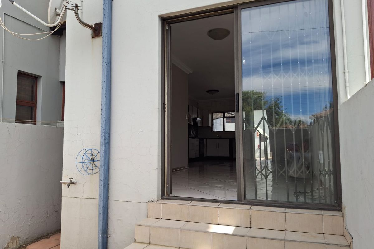 Rear exterior view of a townhouse featuring a sliding glass door with security gate, tiled entrance steps, and visible exterior wall maintenance requirements.