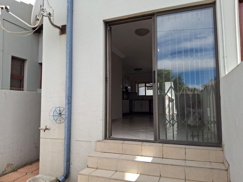 Rear exterior view of a townhouse featuring a sliding glass door with security gate, tiled entrance steps, and visible exterior wall maintenance requirements.