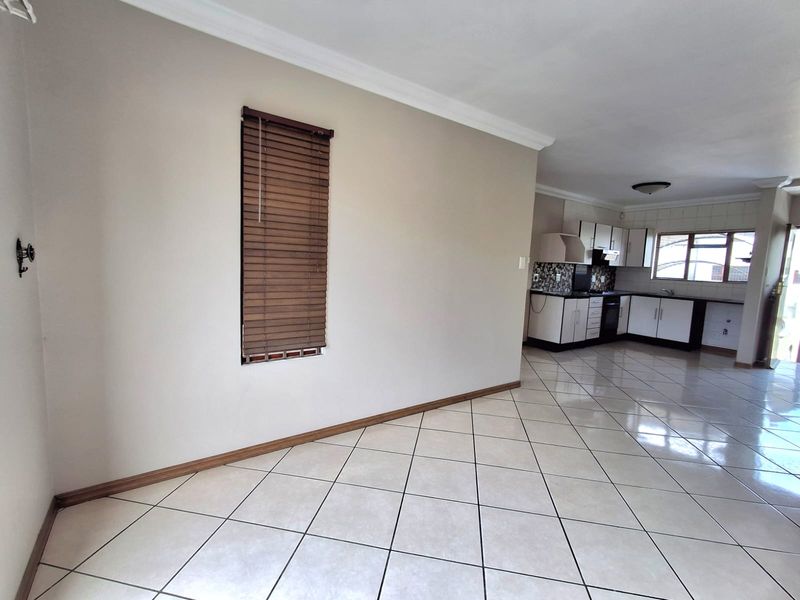 An open-plan living and kitchen area featuring neutral walls, tiled flooring, and functional kitchen cabinetry with built-in appliances.