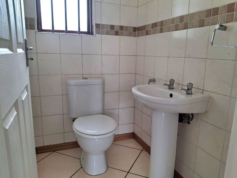 A functional guest bathroom featuring a pedestal basin, toilet, and neutral wall tiling with a decorative mosaic border.