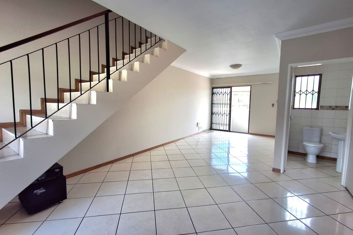 Spacious open-plan living area featuring tiled flooring, a staircase with metal railing, and an adjacent guest bathroom with a pedestal sink.