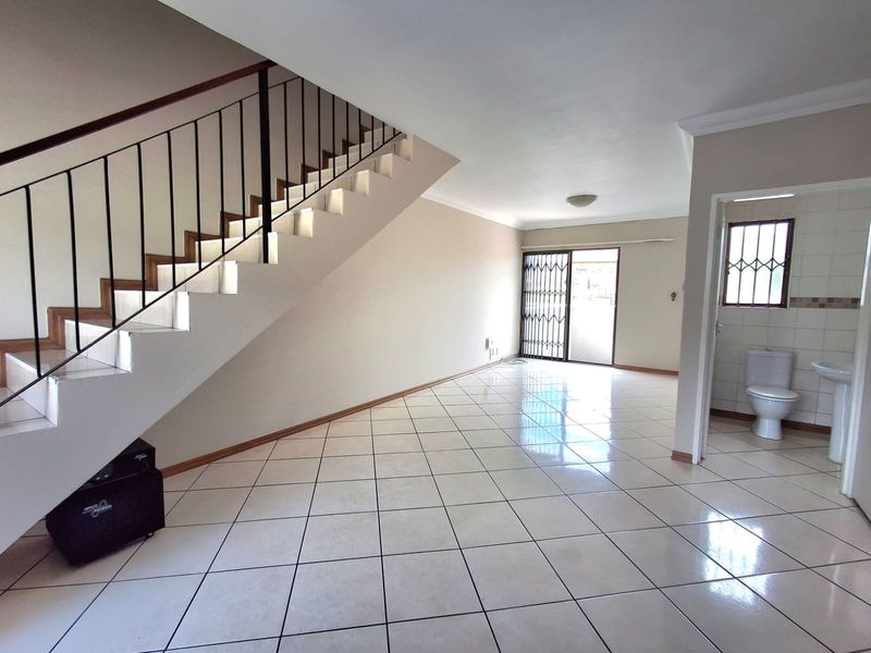 Spacious open-plan living area featuring tiled flooring, a staircase with metal railing, and an adjacent guest bathroom with a pedestal sink.