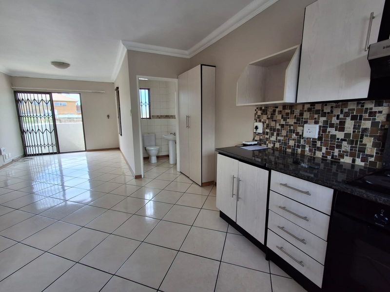Open-plan living area featuring tiled floors, a modern kitchen with granite countertops, and an adjacent bathroom with a toilet and pedestal basin.