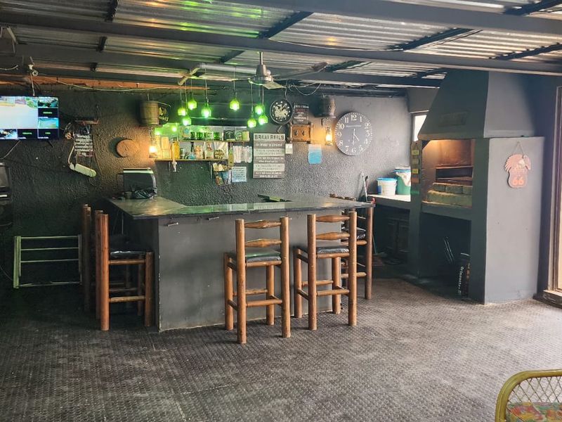 Covered outdoor entertainment area featuring a built-in braai, bar counter, and sliding glass doors leading to the garden.