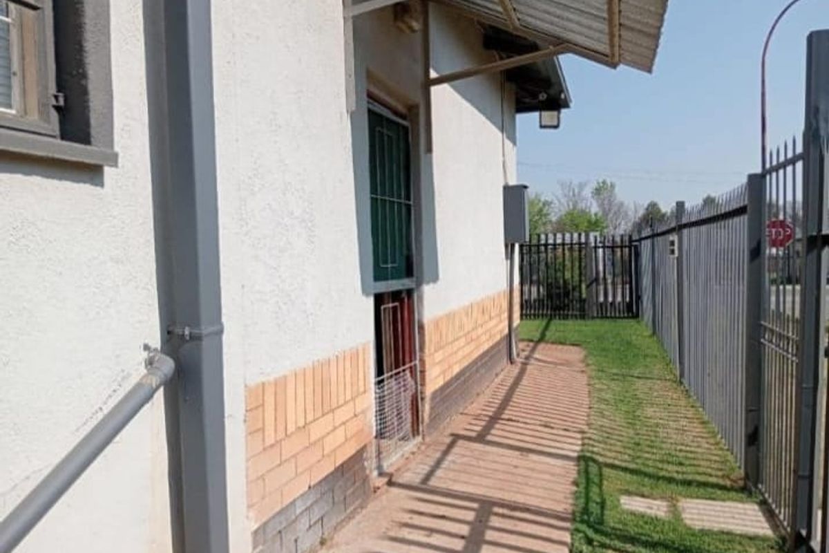 Side exterior view of the property featuring a metal security gate, brick facade, and a small metal awning over the entrance.