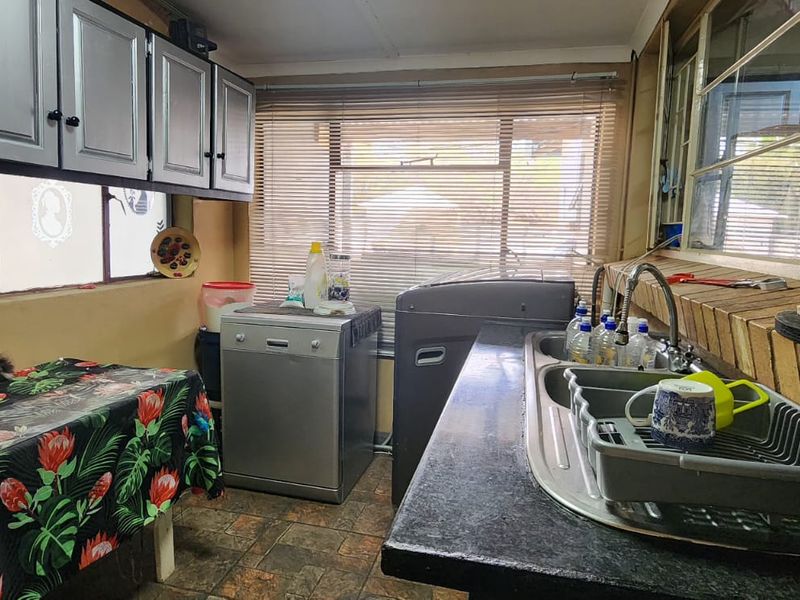 Functional scullery area featuring built-in cabinetry, a stainless steel double sink, and tiled flooring, providing practical space for laundry or kitchen preparation tasks.