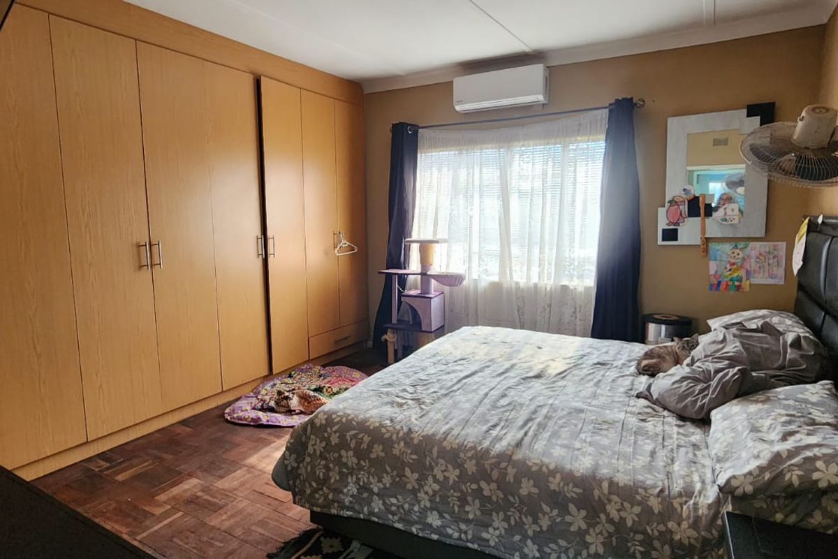 Spacious bedroom featuring warm-toned parquet flooring, extensive built-in wooden cupboards, and a wall-mounted air conditioning unit for climate control.