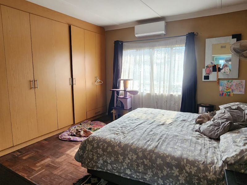 Spacious bedroom featuring warm-toned parquet flooring, extensive built-in wooden cupboards, and a wall-mounted air conditioning unit for climate control.