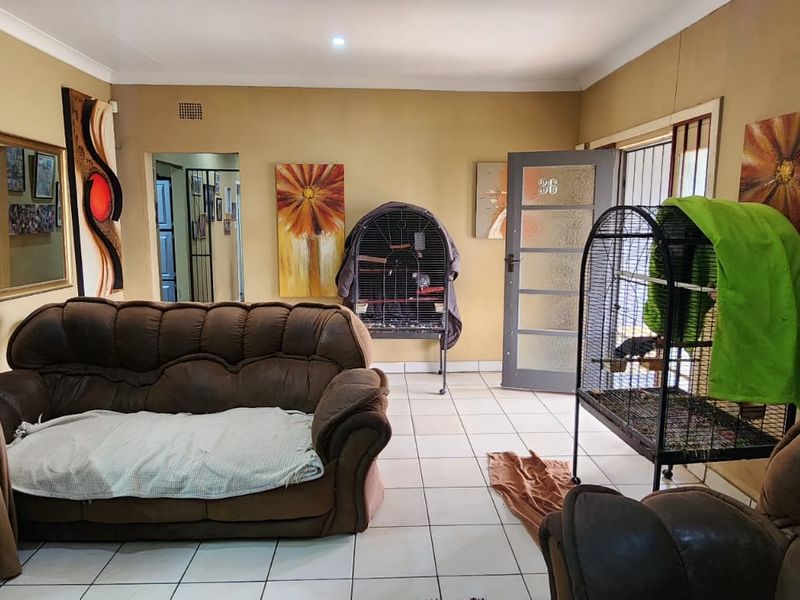 A living room featuring tiled flooring, cove cornicing, and a glass-panelled entrance door with an integrated security gate.