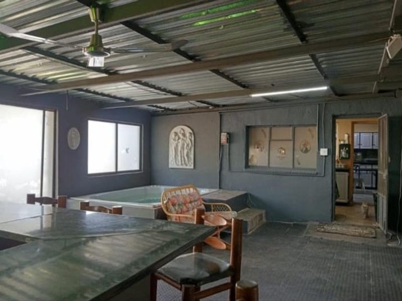 Covered patio area featuring a built-in jacuzzi, bar counter, and corrugated metal roofing, providing a functional space for outdoor entertainment.