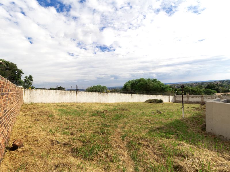 A vacant residential plot featuring a perimeter brick wall with electric fencing and a retaining wall, offering potential for development.