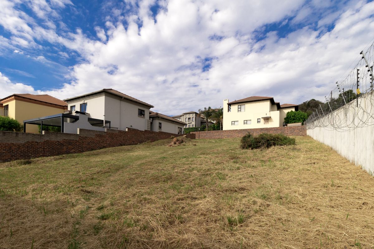 A vacant residential plot featuring established brick boundary walls, concrete retaining walls, and perimeter electric fencing in a developed suburban estate.