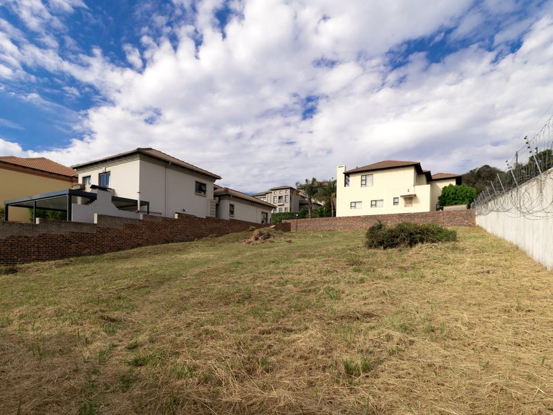 A vacant residential plot featuring established brick boundary walls, concrete retaining walls, and perimeter electric fencing in a developed suburban estate.