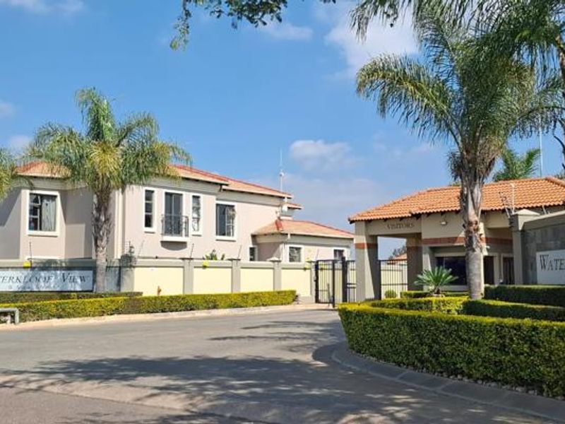 The entrance to Waterkloof View residential estate featuring a gated security access point, perimeter walling, and well-maintained landscaped gardens.