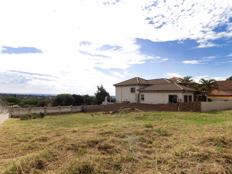 A vacant residential plot featuring perimeter brick boundary walls with electric fencing, offering a clear view of the surrounding neighborhood.