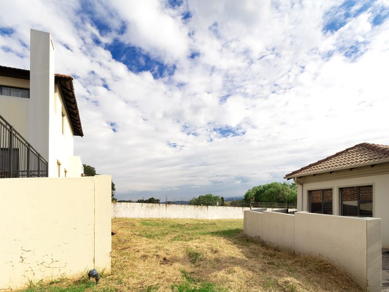 A view of the rear yard area between two residential structures, featuring a perimeter boundary wall and open grass space.