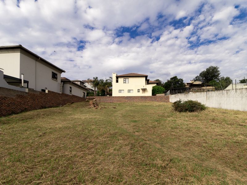 A vacant residential plot featuring established brick and concrete boundary walls with security fencing, offering a clear space for future development.