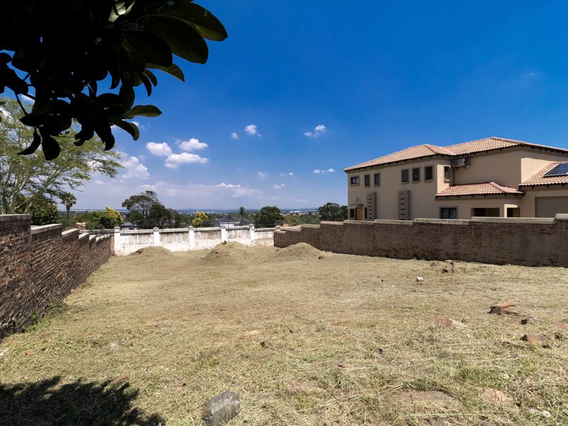 A vacant residential plot featuring established brick boundary walls and a clear view of the surrounding neighborhood.
