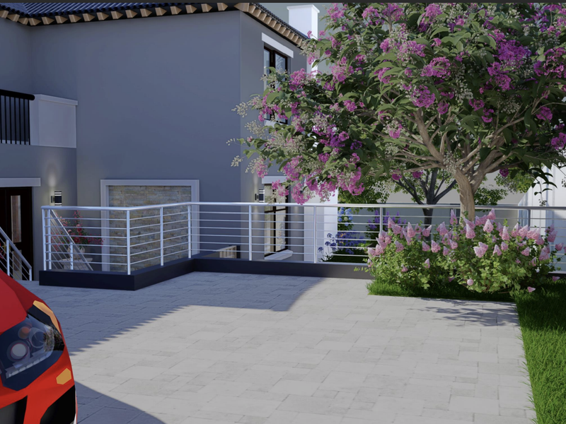 A modern residential exterior featuring a paved driveway, metal safety railings, and landscaped garden areas with mature flowering trees.