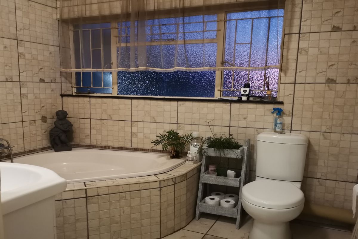 A functional bathroom featuring a corner bathtub, toilet, and vanity basin, finished with dated wall and floor tiling.