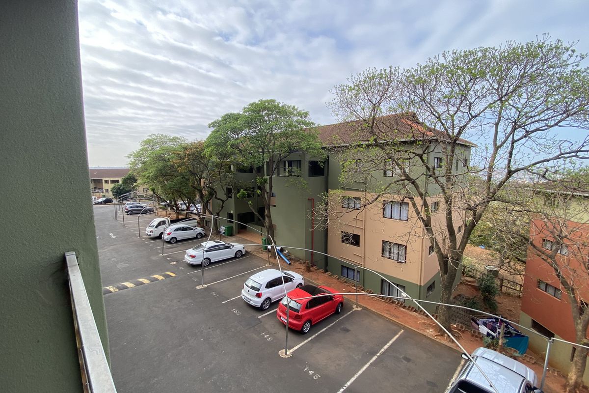 Elevated view of the apartment complex exterior, featuring a paved parking area and multi-story residential building facade.