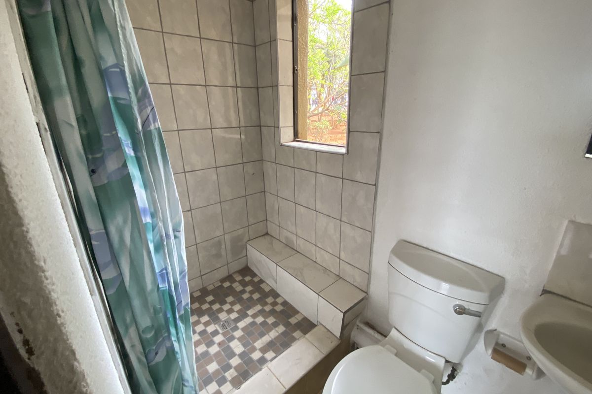 A compact bathroom featuring a tiled shower enclosure with a built-in bench, a standard toilet, and a wall-mounted basin.