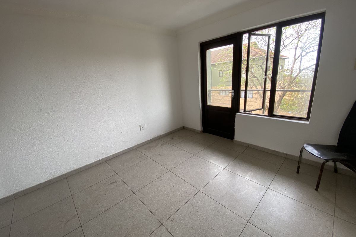 An empty bedroom featuring tiled flooring and direct access to a balcony through a glass-paneled door.