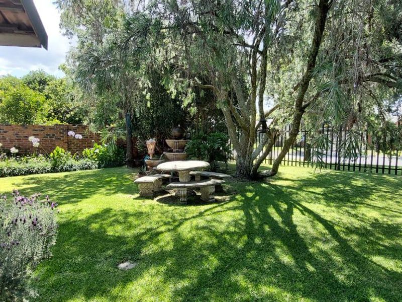 A well-maintained garden area featuring a brick boundary wall, mature trees, and a lawn, viewed from the side of the house.