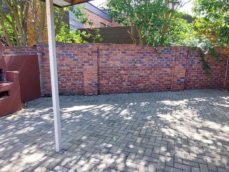 A private outdoor patio area featuring paved flooring, a built-in brick braai, and enclosed by perimeter brick walls.
