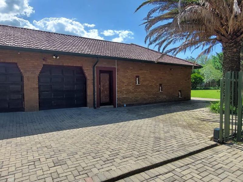 Exterior view of a brick-faced house featuring a double garage, paved driveway, and secure perimeter fencing.