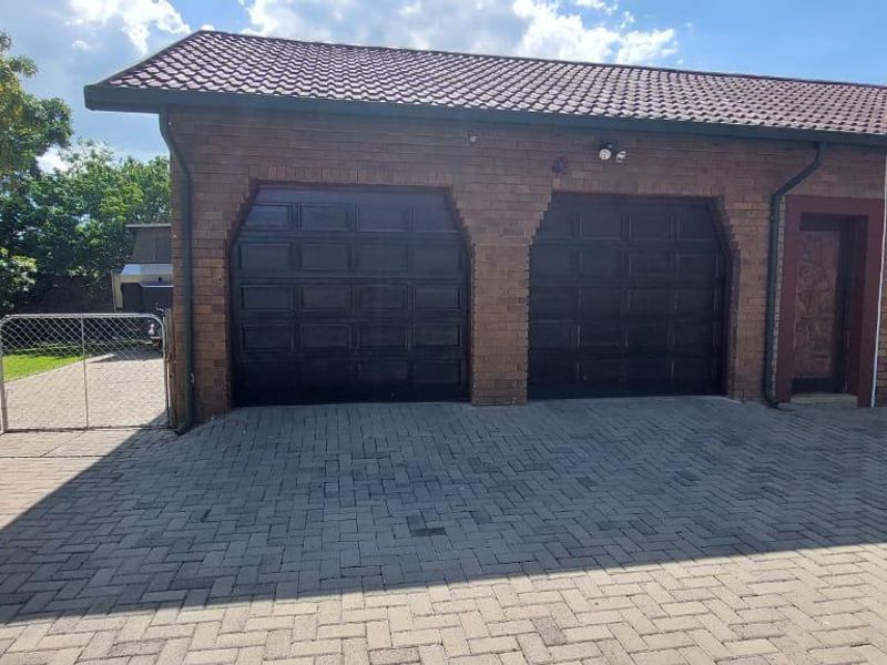A double garage with brick facade, tiled roof, and paved driveway, featuring a side gate entrance to the property.