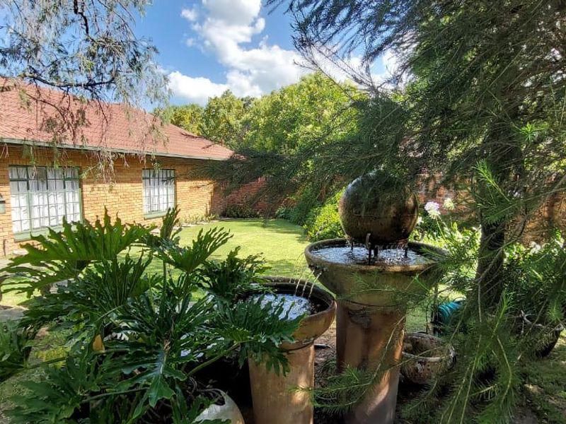 A peaceful rear garden featuring a brick exterior house, established trees, and a decorative stone water fountain.