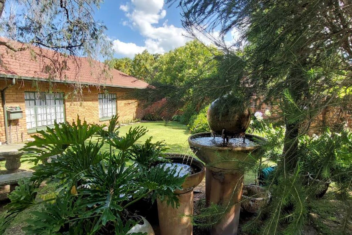 A peaceful rear garden featuring a brick exterior house, established trees, and a decorative stone water fountain.