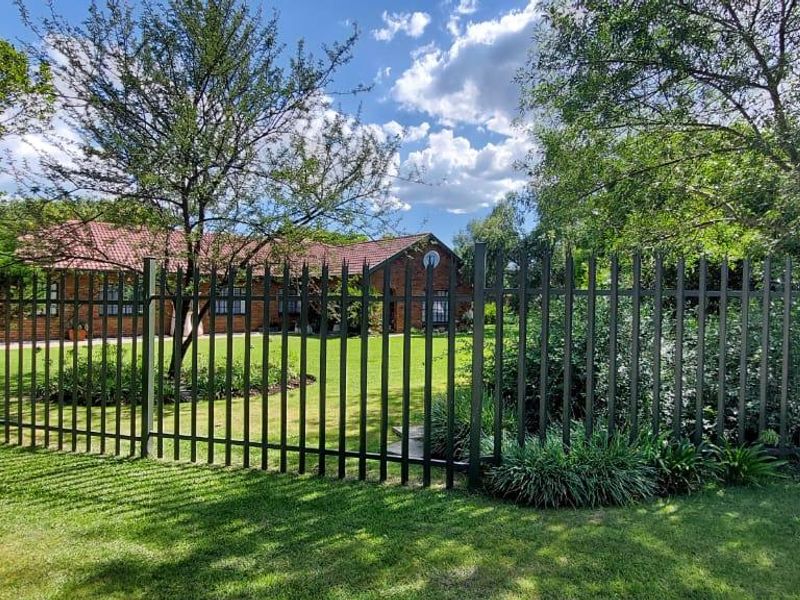 A view of the property's front garden and brick facade, secured by a dark metal perimeter fence and surrounded by mature trees.