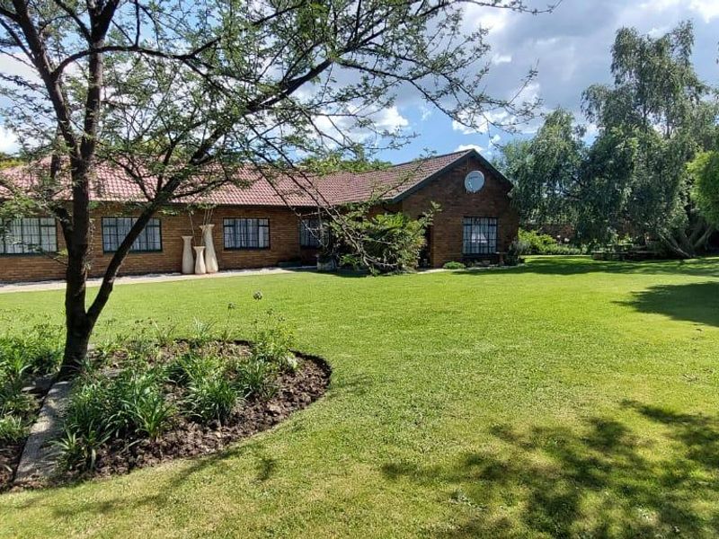 A spacious, well-maintained garden featuring a lush green lawn and mature trees, providing a scenic view of the brick-faced residential property.
