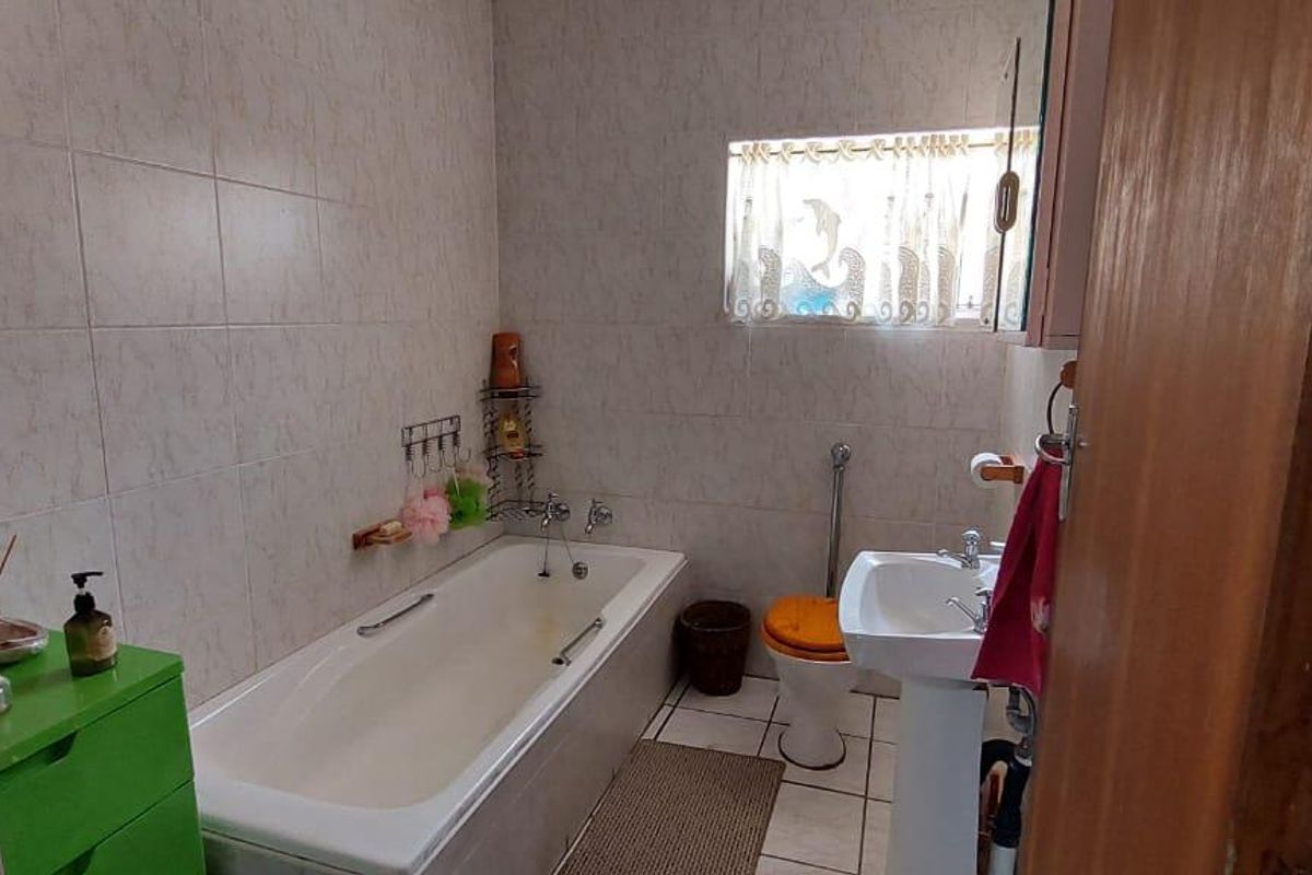 A functional bathroom featuring a standard bathtub, pedestal basin, and toilet with tiled walls and flooring.