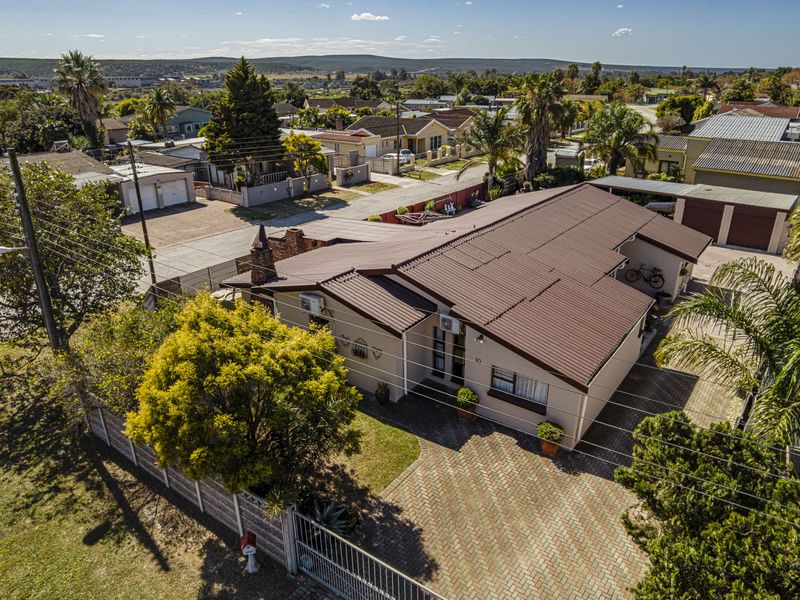 Aerial view of a residential property featuring a brown corrugated metal roof, paved driveway, and perimeter walling in a suburban neighborhood setting.