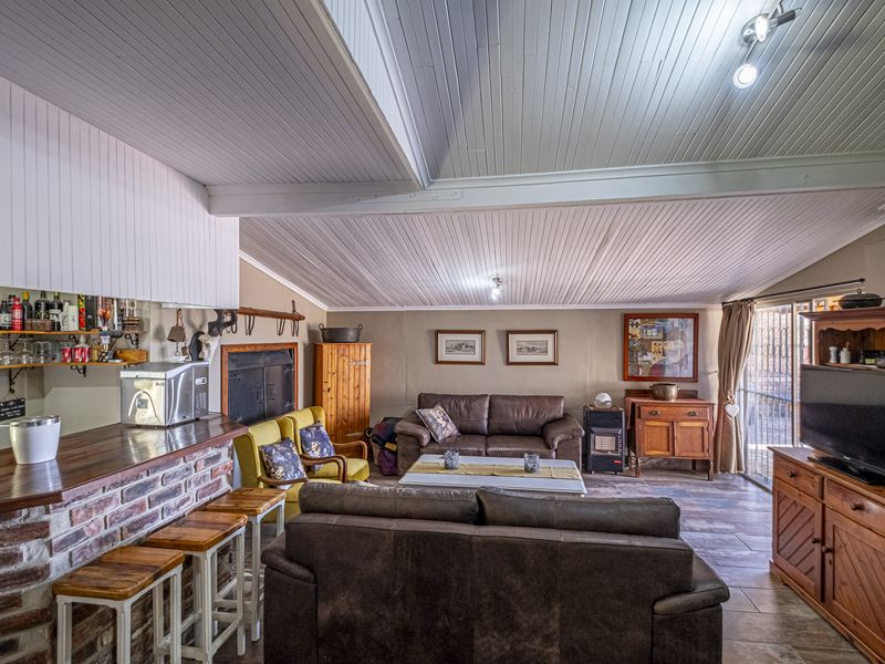 Spacious open-plan living area featuring a brick bar counter, vaulted timber-clad ceilings, tiled flooring, and a built-in fireplace with direct patio access.